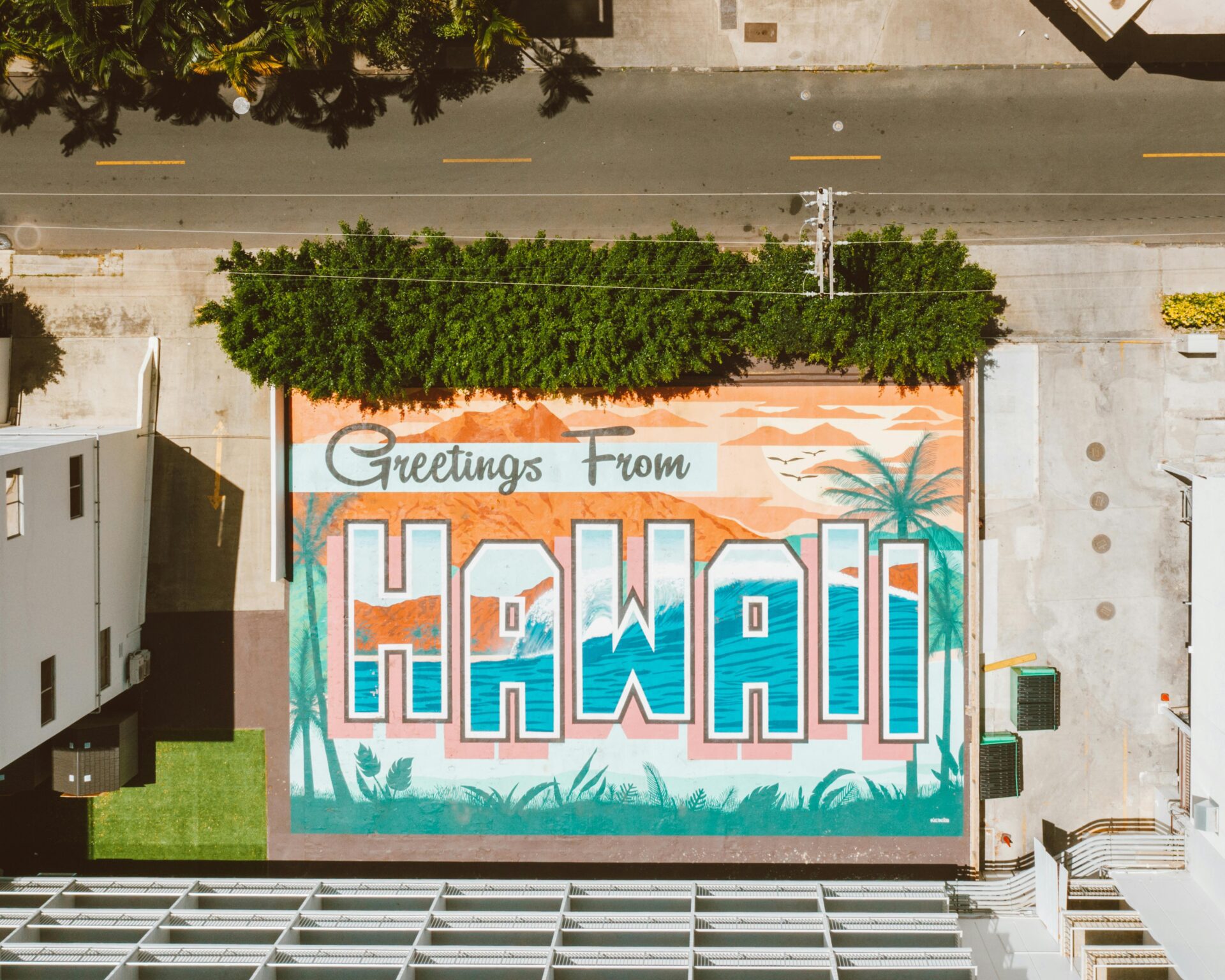 A mural painting on concrete pavement says, “Greetings from Hawaii.”